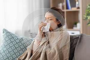 Sick asian woman blowing nose with tissue at home