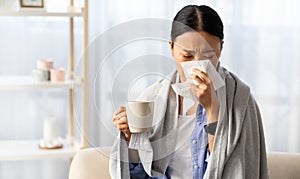 Sick asian woman have cold or flu, sitting on couch at home