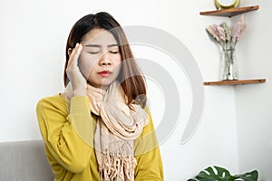 Sick Asian woman having headache, migraine sitting on sofa , woman have fever in winter season