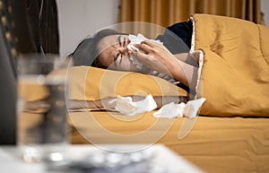 Sick asian woman is ill with a cold flu or sinus virus disease,sinusitis ,runny nose is blowing her nose,sneezing with paper