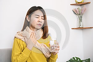 Sick Asian woman suffering from sore throat hand holding glass of hot water