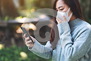 A sick asian woman wearing protective face mask, using mobile phone for Healthcare and Covid-19 concept