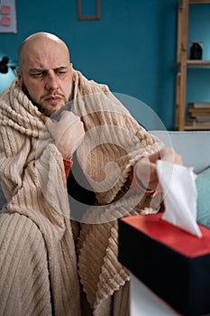 Sick attractive man have a fever, flu and take tissues paper sneezing nose, runny while sitting on sofa