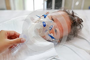 Sick baby boy applying inhale medication by inhalation mask to cure Respiratory Syncytial Virus RSV on patient bed at hospital photo