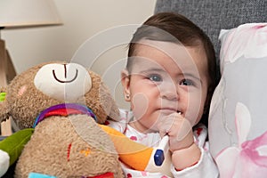 Sick baby girl with thermometer in mouth holding teddy bear