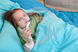 A sick baby lying in bed and looking at thermometer