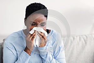 Sick black woman sneezing, holding tissue paper