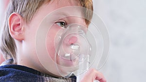 Sick blond boy inhaling through inhaler mask, close-up face side view. Use nebulizer and inhaler for the treatment.