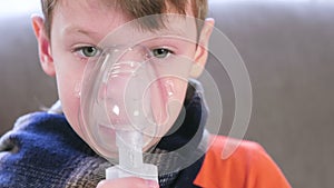 Sick blond boy inhaling through inhaler mask, close-up face. Use nebulizer and inhaler for the treatment.