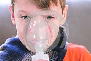 Sick blond boy inhaling through inhaler mask. Use nebulizer and inhaler for the treatment.