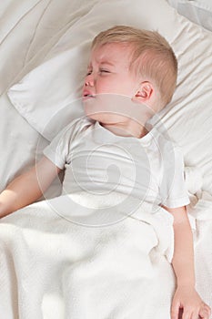 A sick blond toddler wearing white t-shirt lying