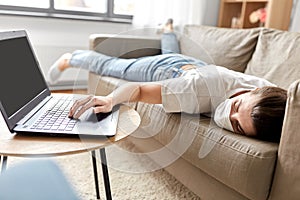 Sick bored woman with laptop lying on sofa at home