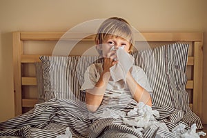 Sick boy coughs and wipes his nose with wipes. Sick child with fever and illness in bed