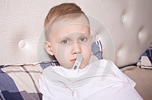 Sick boy with digital thermometer. Ill boy is measuring body temperature and doesn t feel well photo