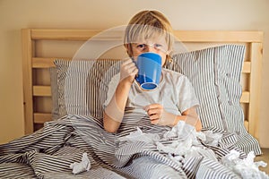 Sick boy drinking tea in his bed. Sick child with fever and illness in bed