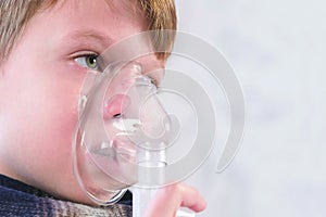 Sick boy inhaling through inhaler mask, face close-up side view. Use nebulizer and inhaler for the treatment.