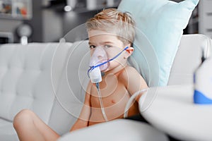 Sick boy in nebulizer mask making inhalation, respiratory procedure by pneumonia or cough for child, inhaler, compressor