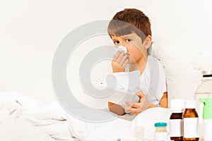 Sick boy sitting in bed and using paper napkins