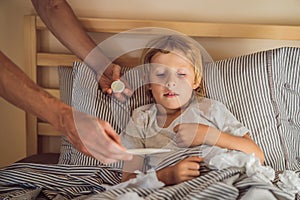 Sick boy with thermometer laying in bed and father hand taking temperature. father checking temperature of her sick son