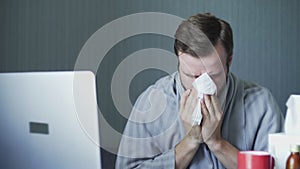 Sick business man working with laptop computer and documents at home. Man blowing his nose