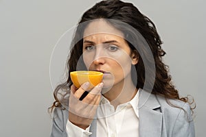 Sick business woman trying to sense smell of half fresh orange, has symptoms of Covid-19