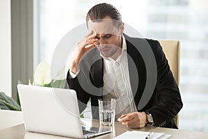 Sick businessman having severe headache, holding painkiller reme