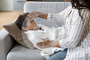 Sick Child. Black mother touching son& x27;s forehead, checking his temperature at home