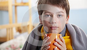 Sick child boy drinking hot tea to recover from flu. sitting in bed a at home