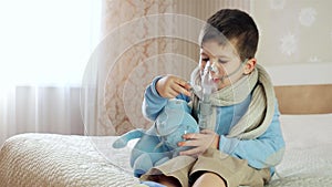 Sick child breathes through nebulizer, baby does inhalation, boy with an oxygen mask on his face, treatment at home