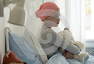 Sick child with cancer sitting in hospital bed photo