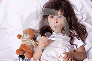 Sick child with fever and illness in bed checking temperature with thermometer. Kids flu treatments. Insurance concept.