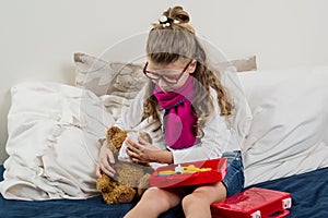 Sick child girl in glasses, heals his sick Teddy bear