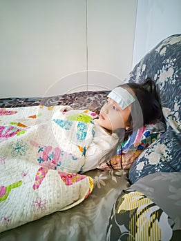 Sick child with high fever laying in bed. Compress gel on forehead