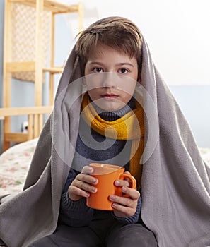 Sick child sitting on bed a at home boy drinking hot tea to recover from flu