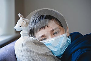 Sick child wearing a protective mask, ill kid in a medical face mask lying head on sofa with sad face,Upset boy sitting on couch