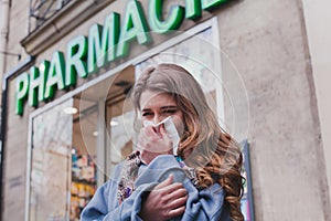 Sick cold woman next to a pharmacy, flu concept