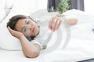 Sick cute teen girl lying in bed with termometer in her hand