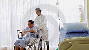 Sick elderly asian senior man sitting in bed and walk to wheelchair in hospital with the woman doctor suggestion.