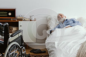 Sick elderly man wearing blue pajama lying in bed at nursing home