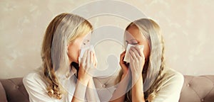 Sick exhausted middle-aged woman mother and adult daughter together sneezing blow nose using tissue