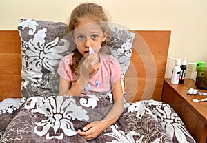 A sick girl buries herself with drops in her nose while lying in bed. Self-treatment