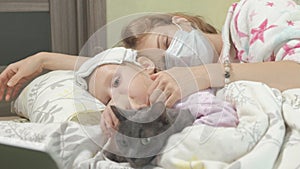 Sick girl with fever Child with fever lying in bed with mother and cat