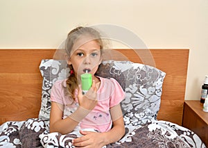 A sick girl holds a spray in her hand and irrigates their throat while lying in bed. Self-treatment photo