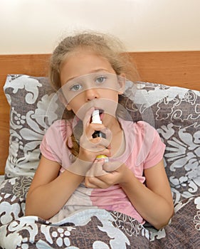 A sick girl holds a spray in her hands and irrigates their throats while sitting in bed. Self-treatment photo