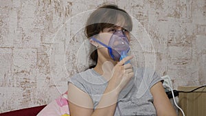 A sick girl is inhaled by a nebulizer sitting on a sofa. The woman in the mask. Inhale vapors for the respiratory tract