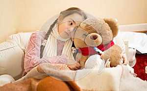 Sick girl resting in bed with brown teddy bear