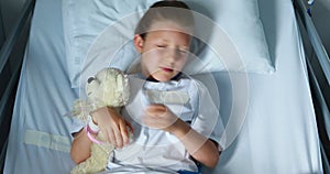 Sick girl resting with teddy bear on bed