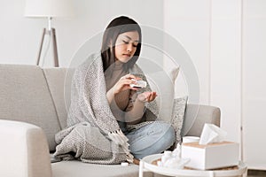 Sick girl taking pills from flu, sitting on sofa