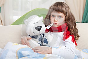 Sick girl with thermometer embraces toy in bed