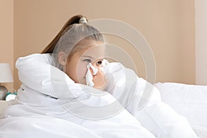 Sick girl with tissue blowing her nose in bed indoors, space for text. Cold symptoms